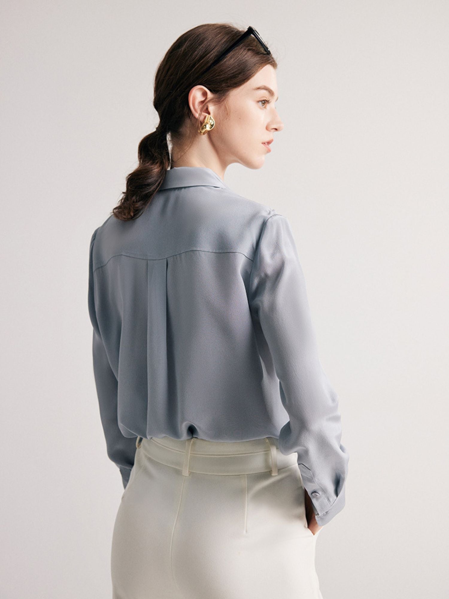 A woman wearing a light blue-colored, long-sleeved, striped silk blouse with a classic collar, paired with a beige skirt.