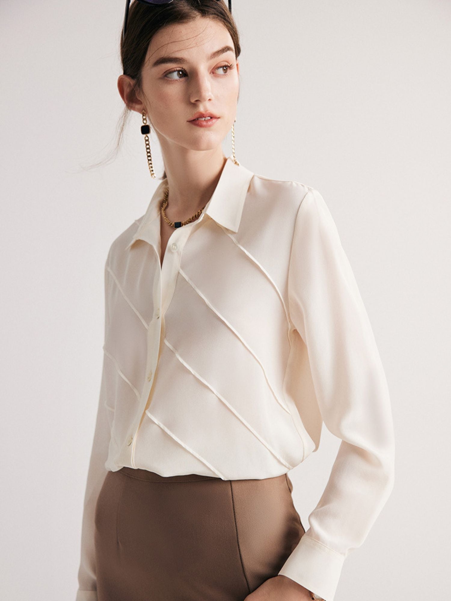 A woman wearing a cream-colored, long-sleeved, striped silk blouse with a classic collar, paired with a beige skirt.