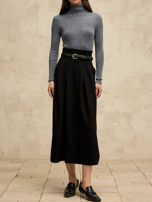 A woman wearing a high-waisted midi length black skirt with a flared silhouette and a belt detail. She has paired it with a gray turtleneck sweater.