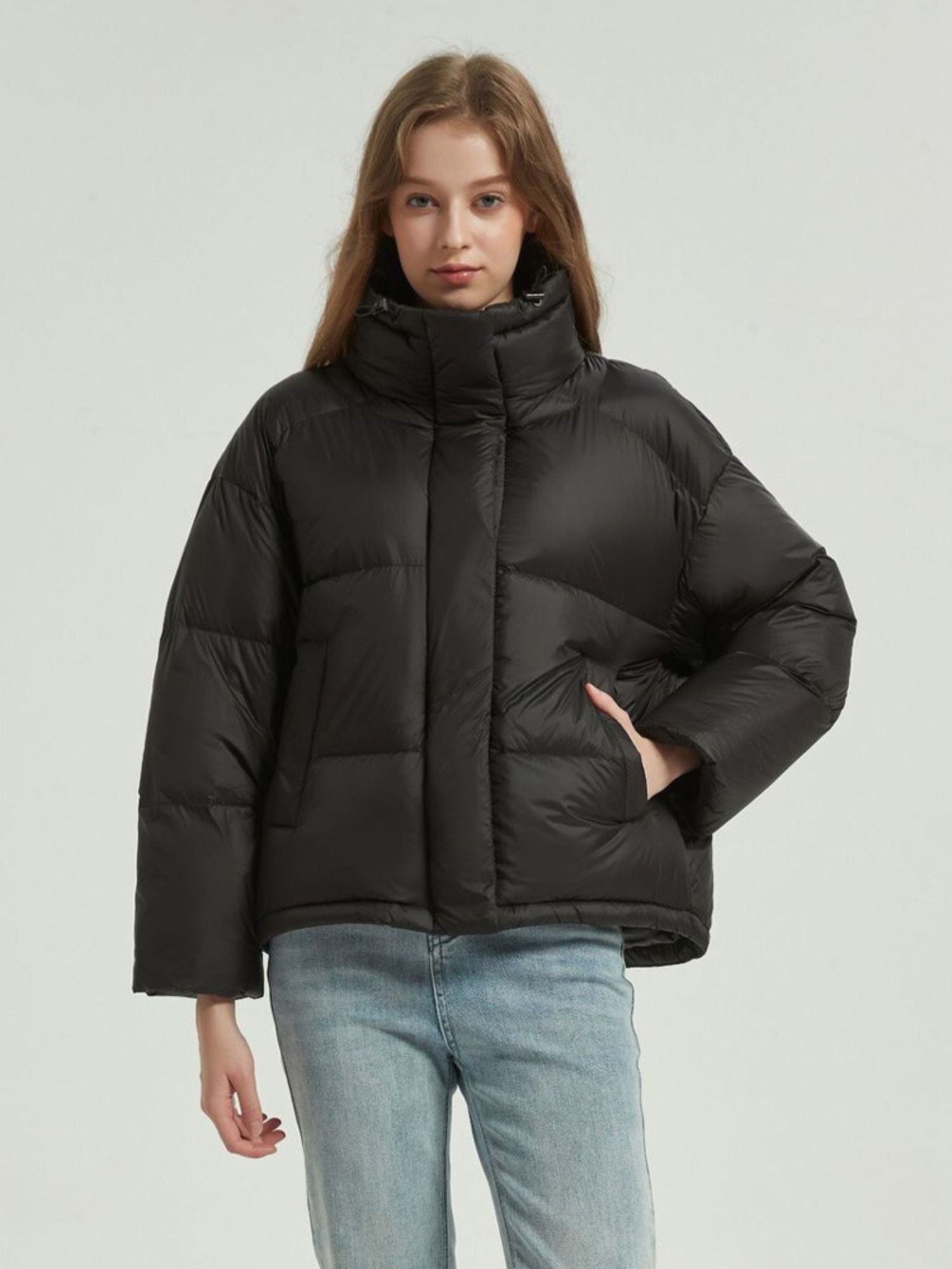 A female model wearing a black reversible quilted down jacket with a stand collar, full zip, and functional pockets.