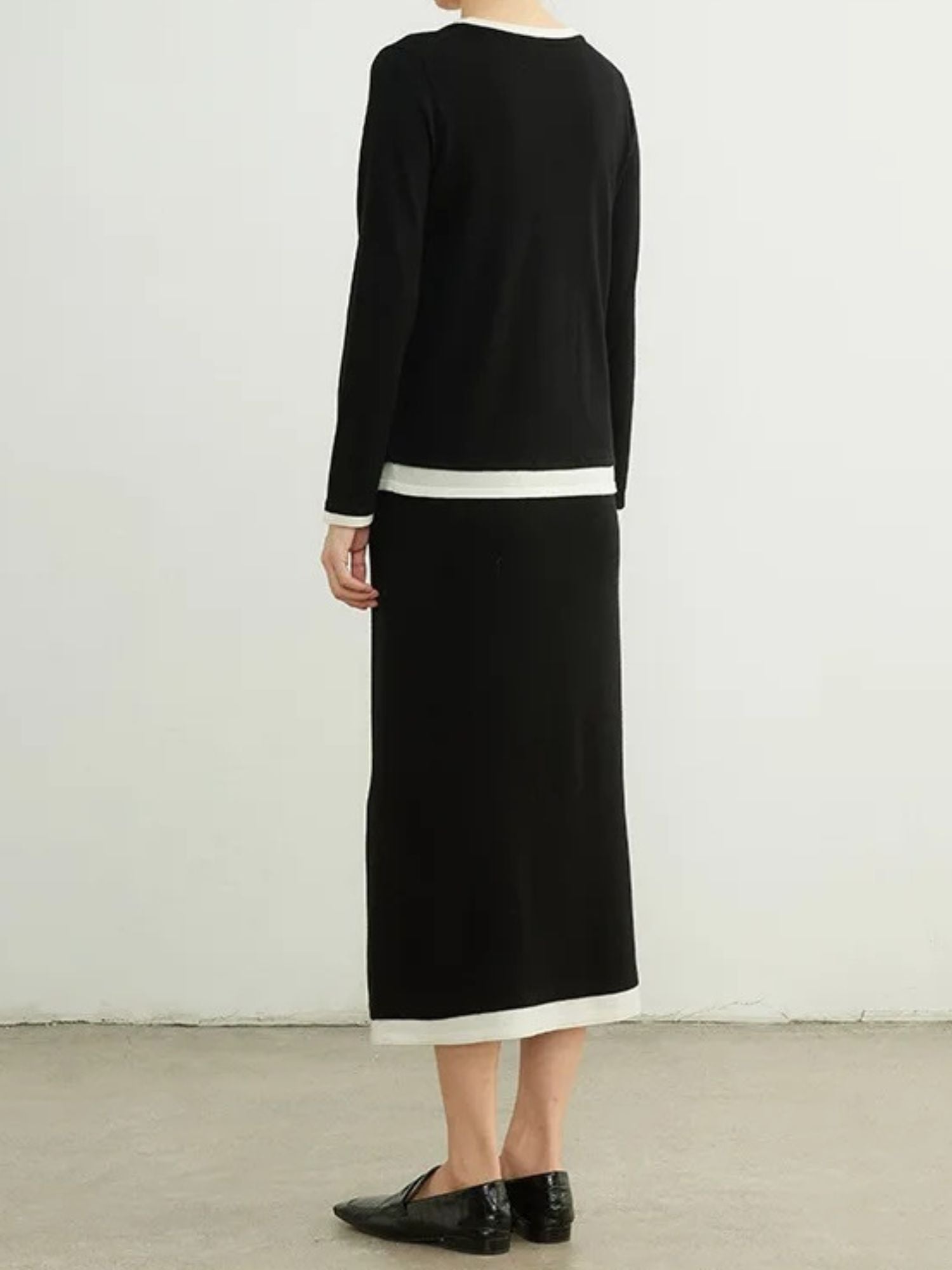 A woman wearing a black sweater and black skirt facing away