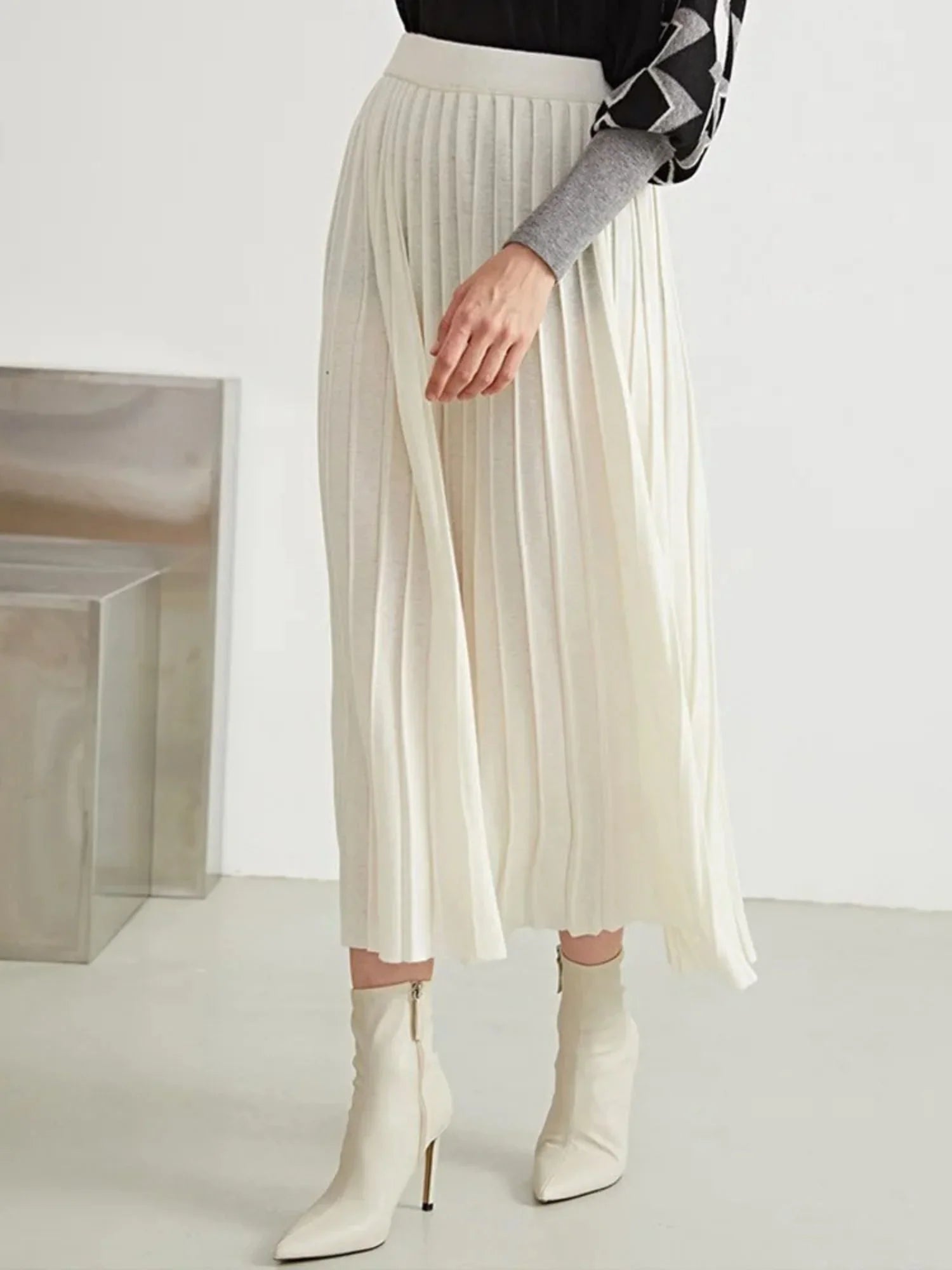 A woman wearing a black and white geometric patterned sweater paired with a pleated long skirt in a beige wool blend.