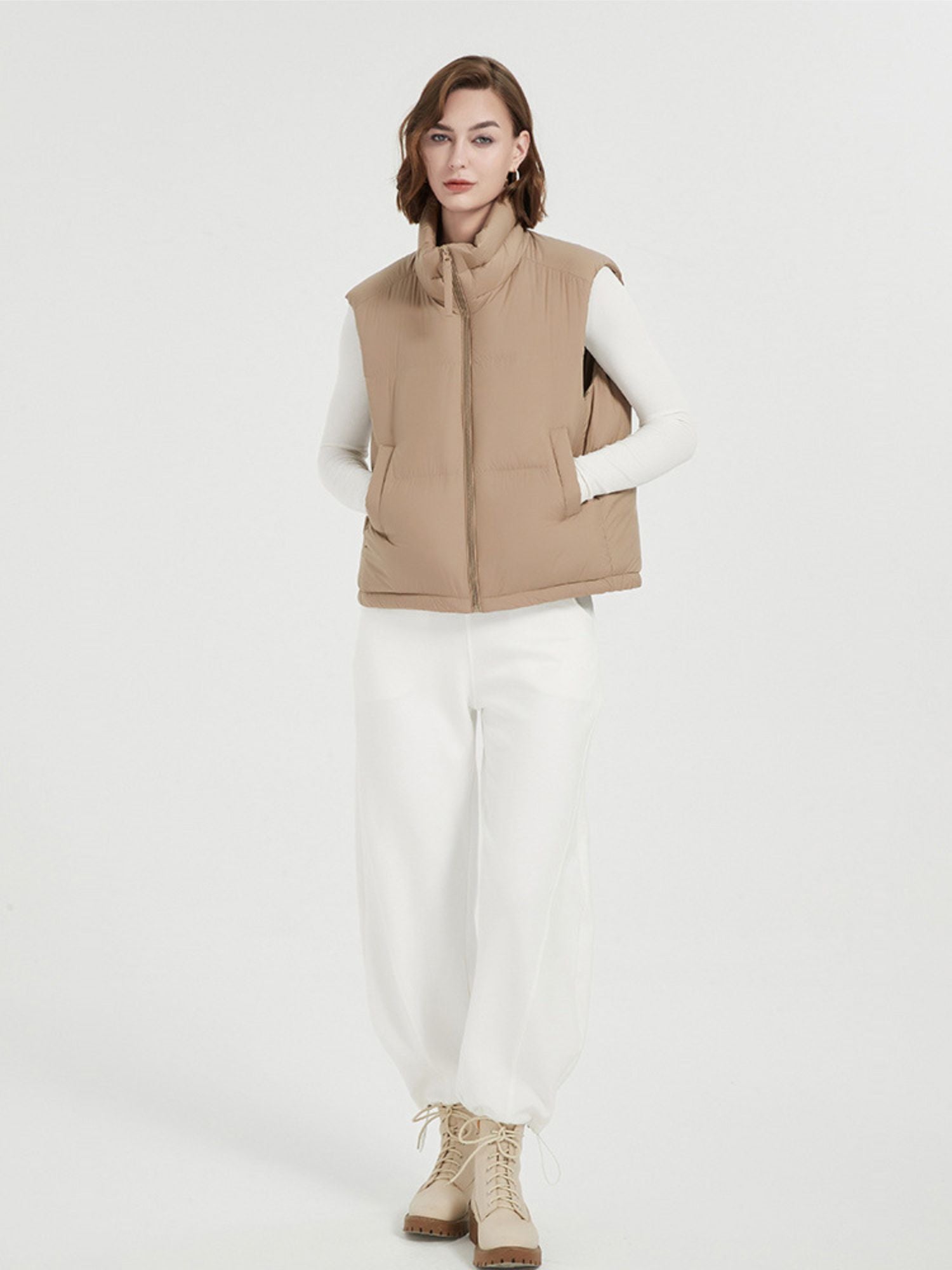 A female model wearing a beige quilted down vest with a stand collar, sleeveless design, and a full zip.