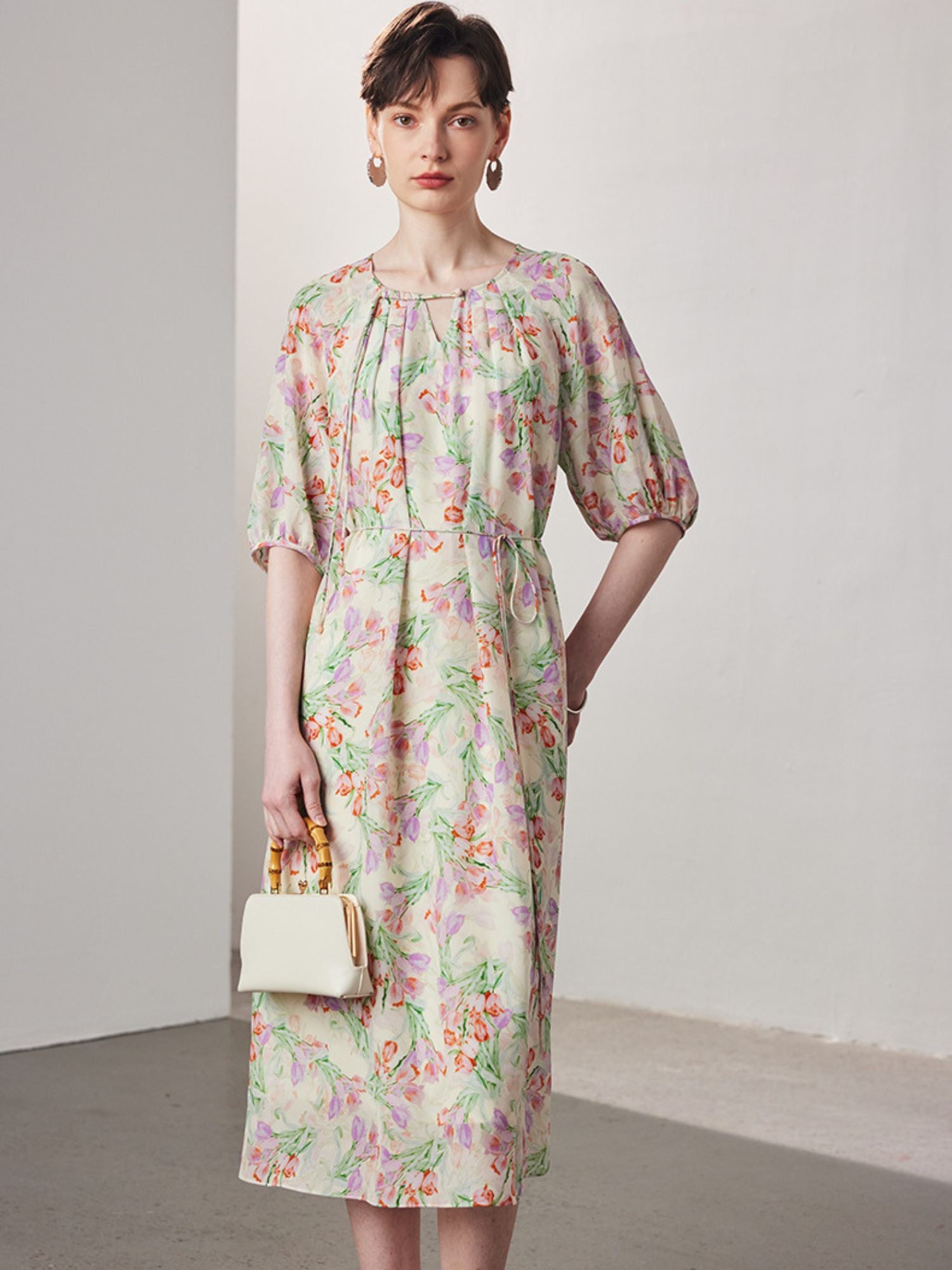 A woman wearing a floral dress wih a white hand bag.