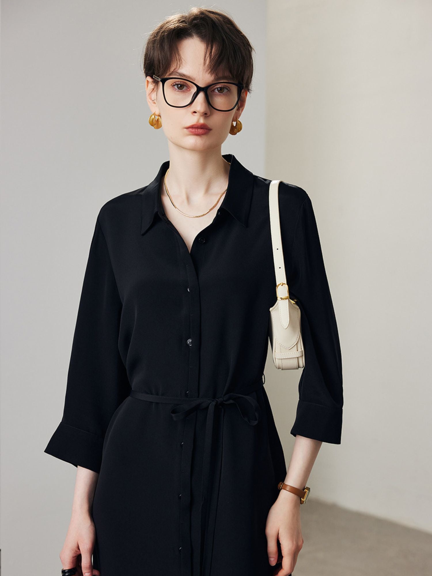 A woman with short hair wearing a lose dress shirt in black and glasses.