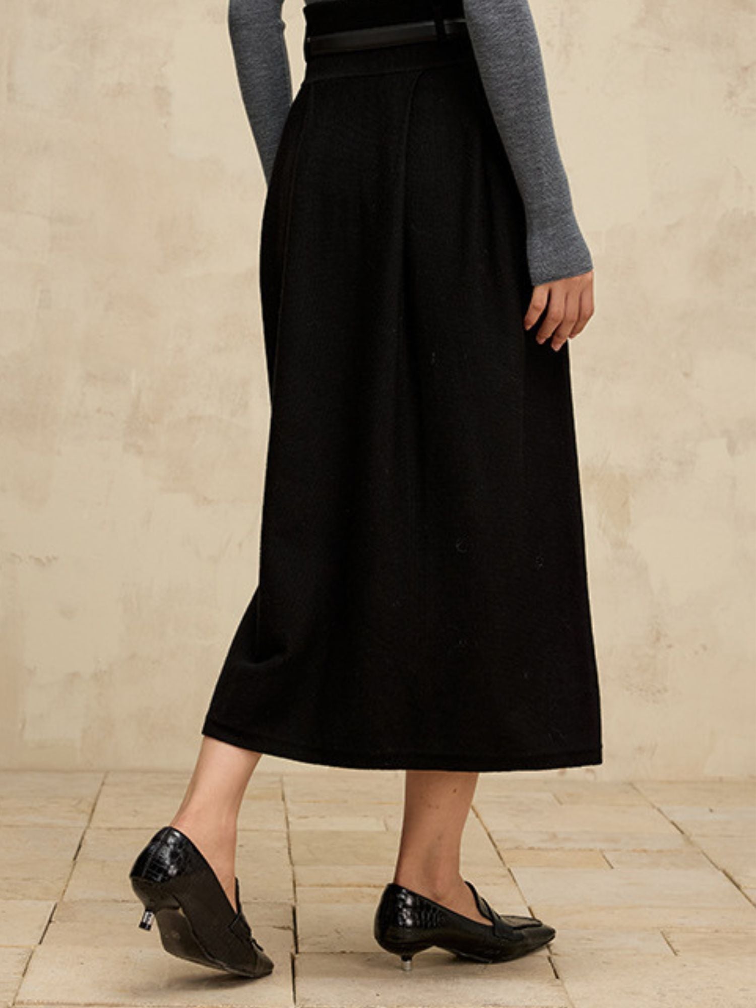 A woman wearing a high-waisted midi length black skirt with a flared silhouette and a belt detail.