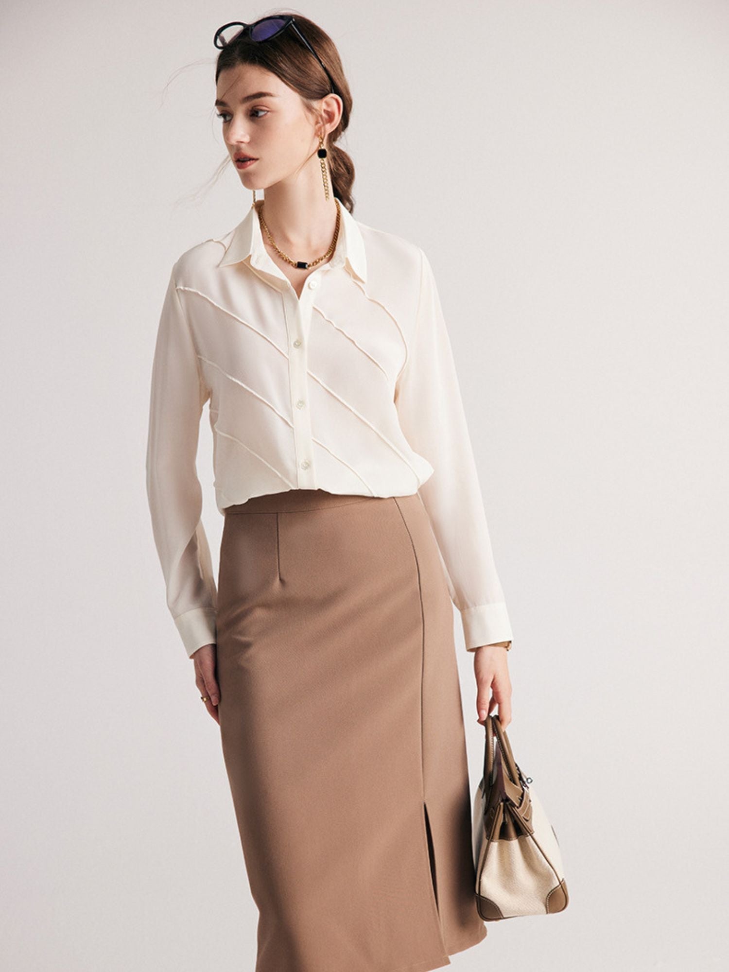 A woman wearing a cream-colored, long-sleeved, striped silk blouse with a classic collar, paired with a beige skirt.