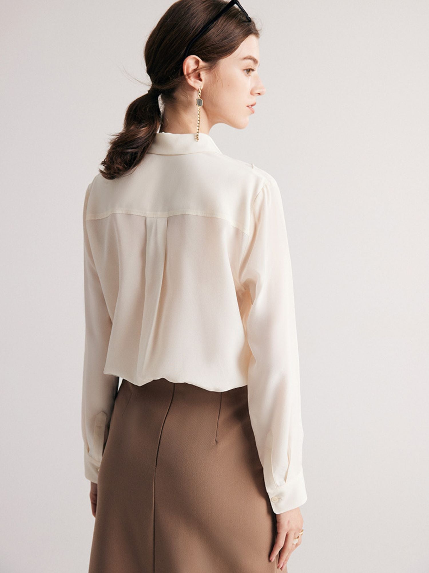 A woman wearing a cream-colored, long-sleeved, striped silk blouse with a classic collar, paired with a beige skirt.