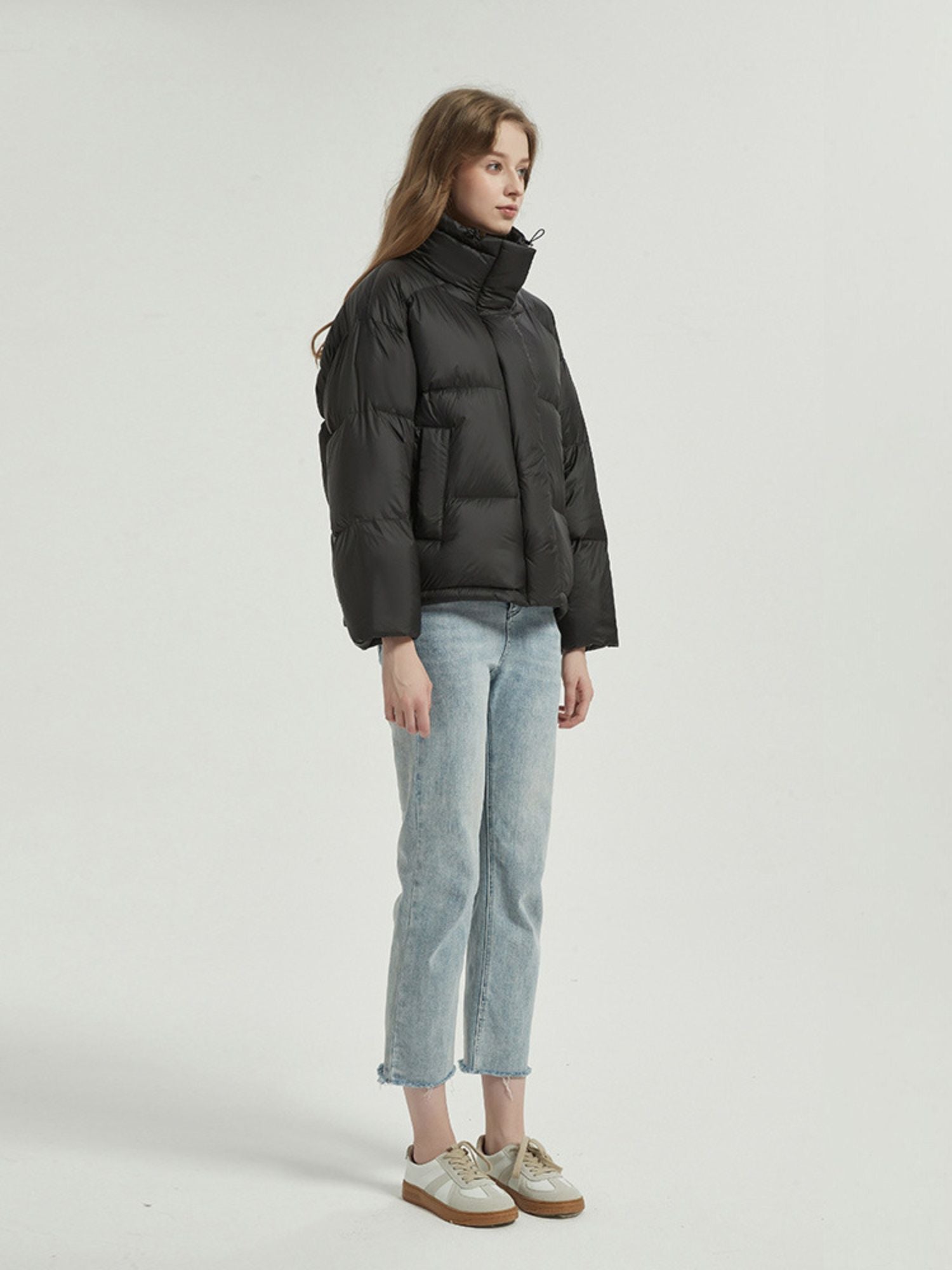 A female model wearing a black reversible quilted down jacket with a stand collar, full zip, and functional pockets.