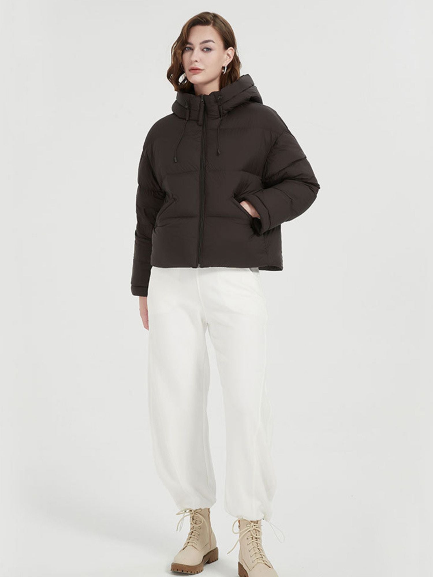 A female model wearing a black quilted down jacket with a hood and functional pockets in a winter setting.
