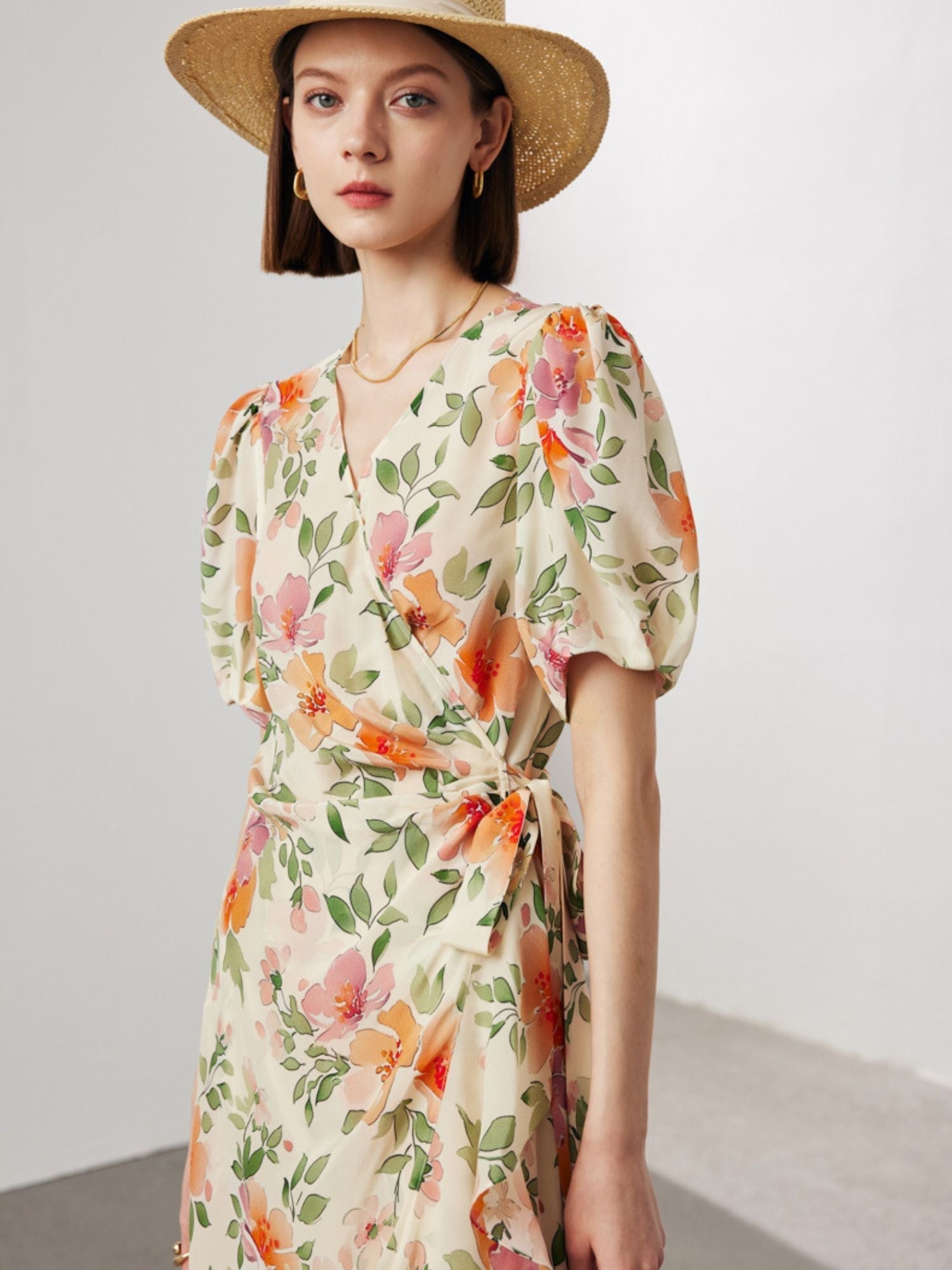 A woman wearing a wrap around floral dress with a hat.