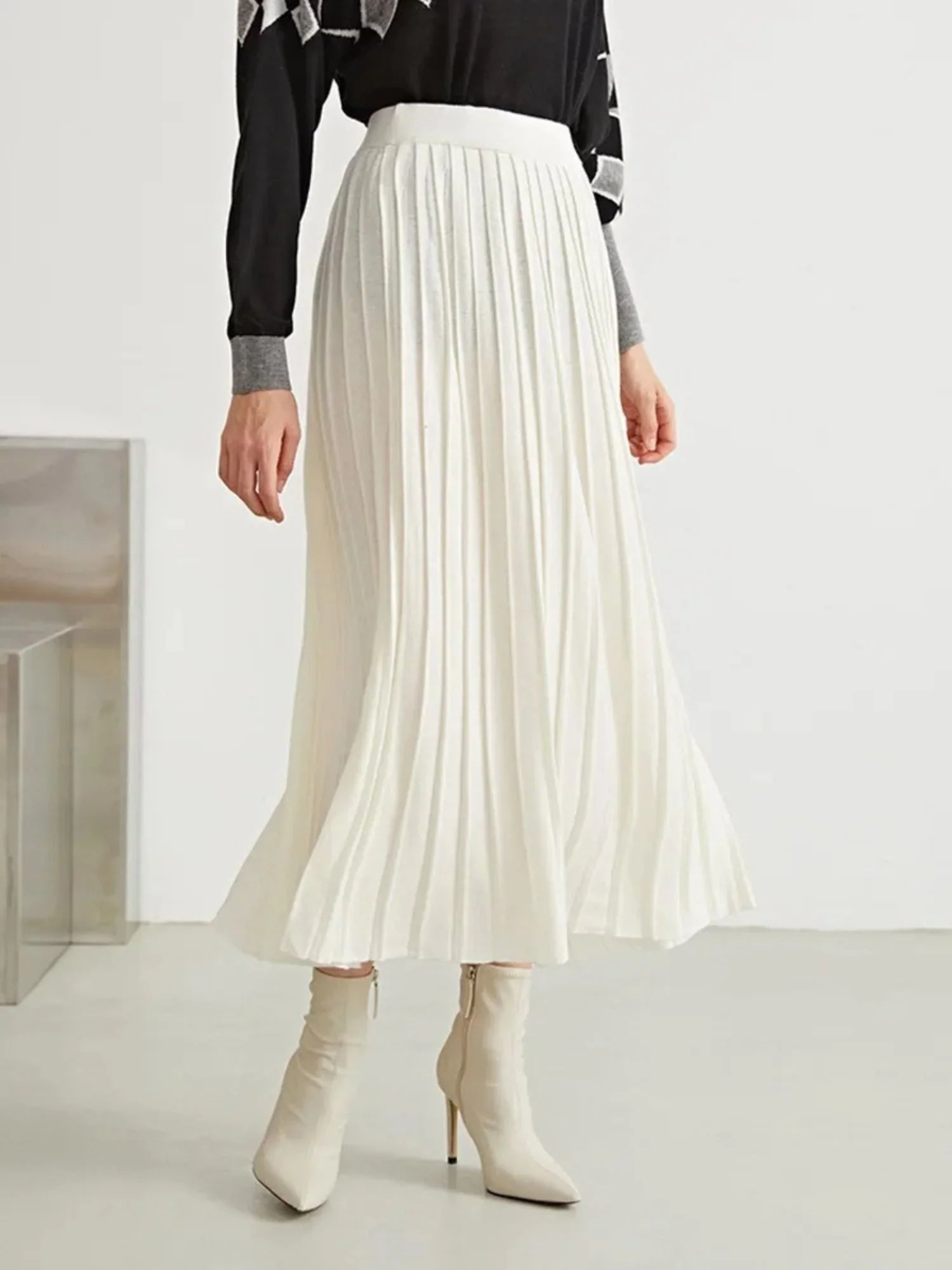 A woman wearing a black and white geometric patterned sweater paired with a pleated long skirt in a beige wool blend.