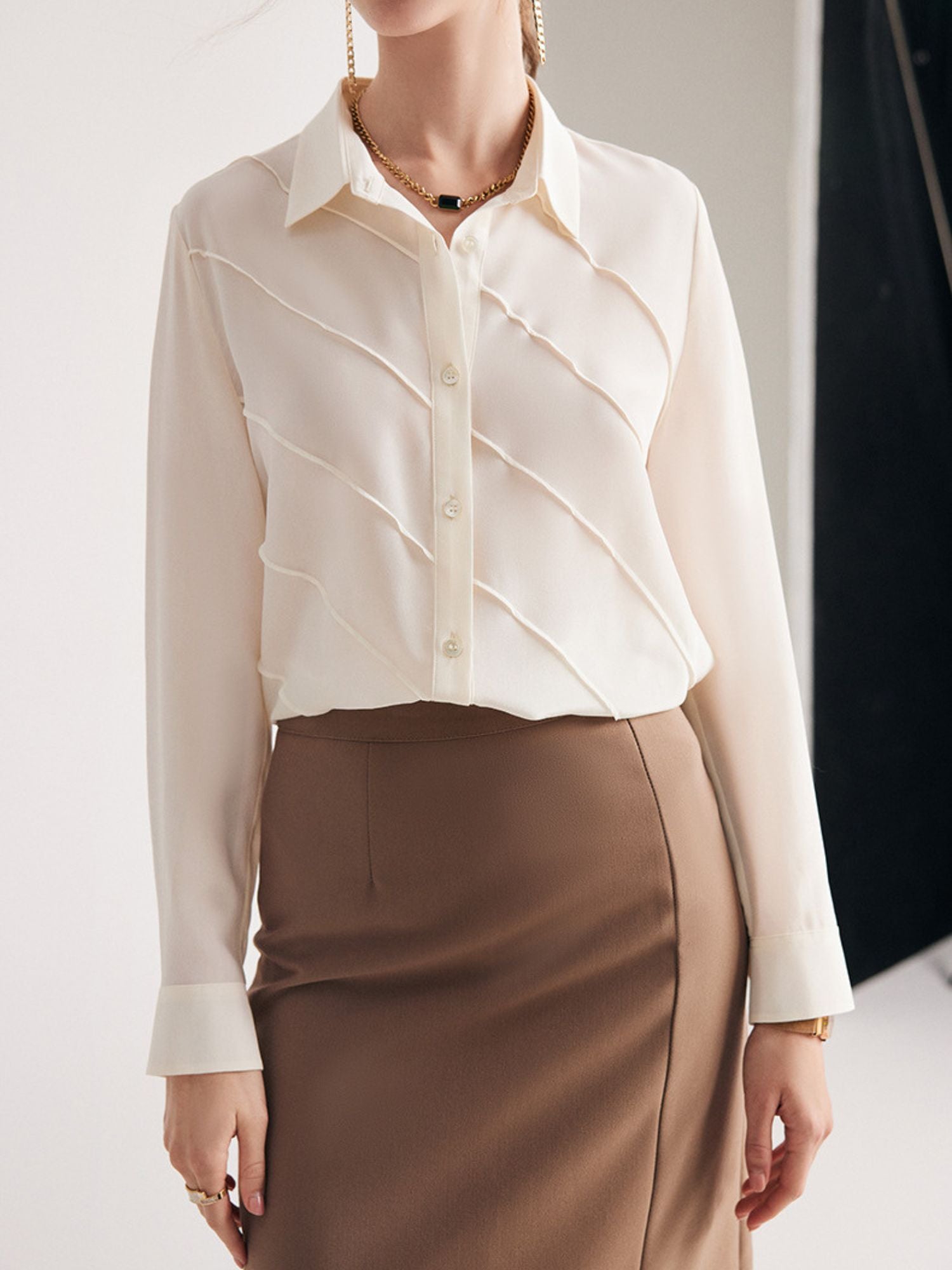 A woman wearing a cream-colored, long-sleeved, striped silk blouse with a classic collar, paired with a beige skirt.