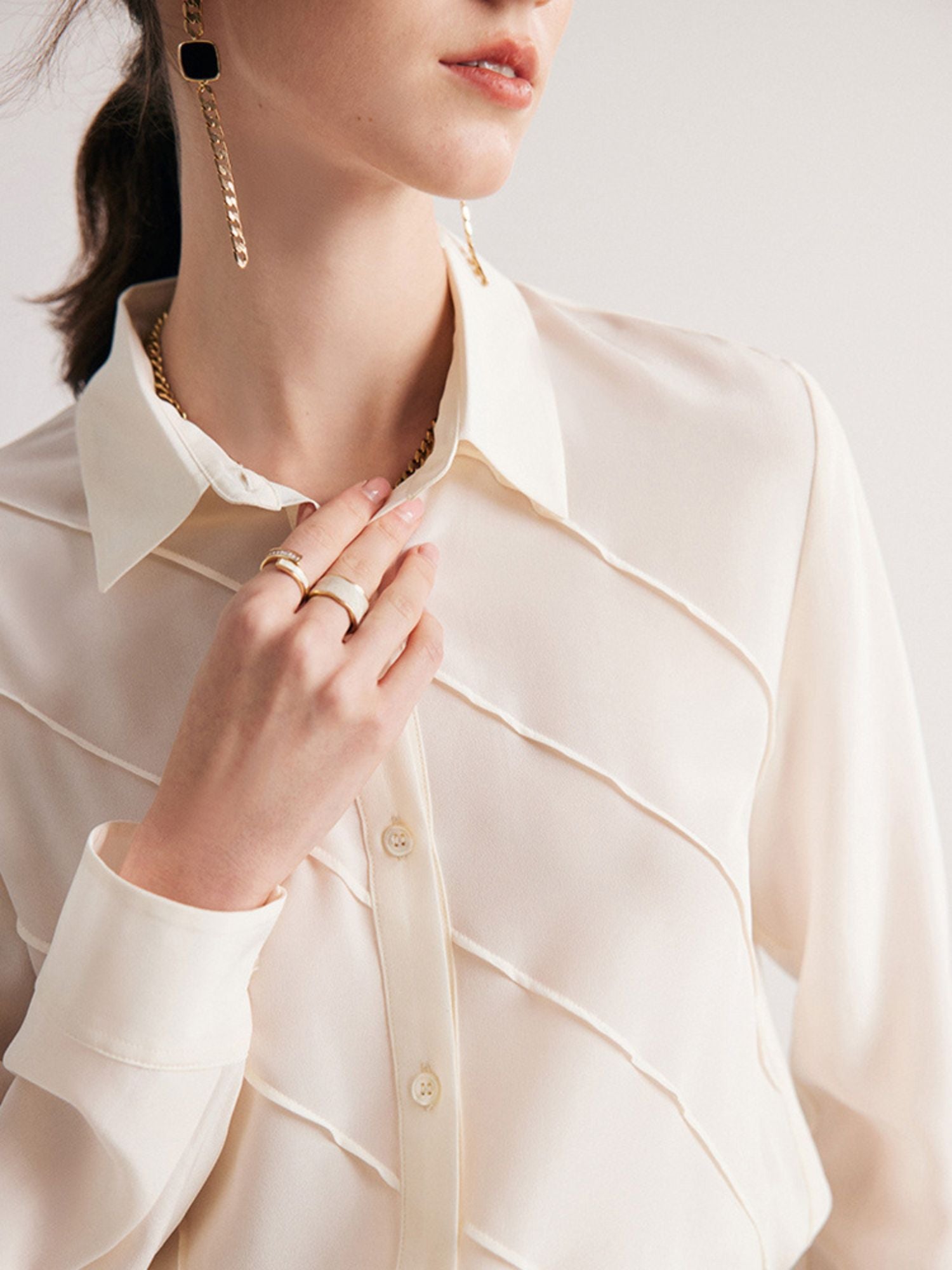Close up of A woman wearing a cream-colored, long-sleeved, striped silk blouse with a classic collar, paired with a beige skirt.