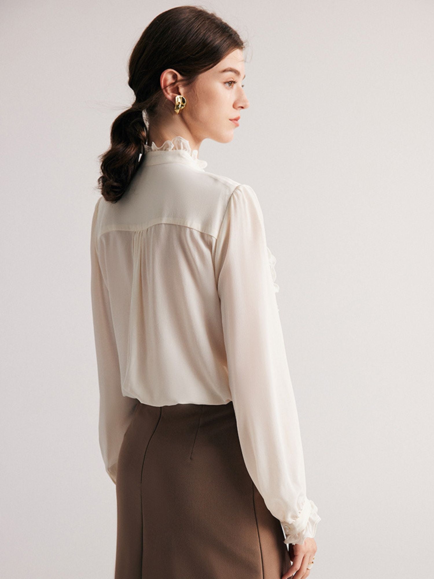 A woman wearing a ruffled white blouse facing away.